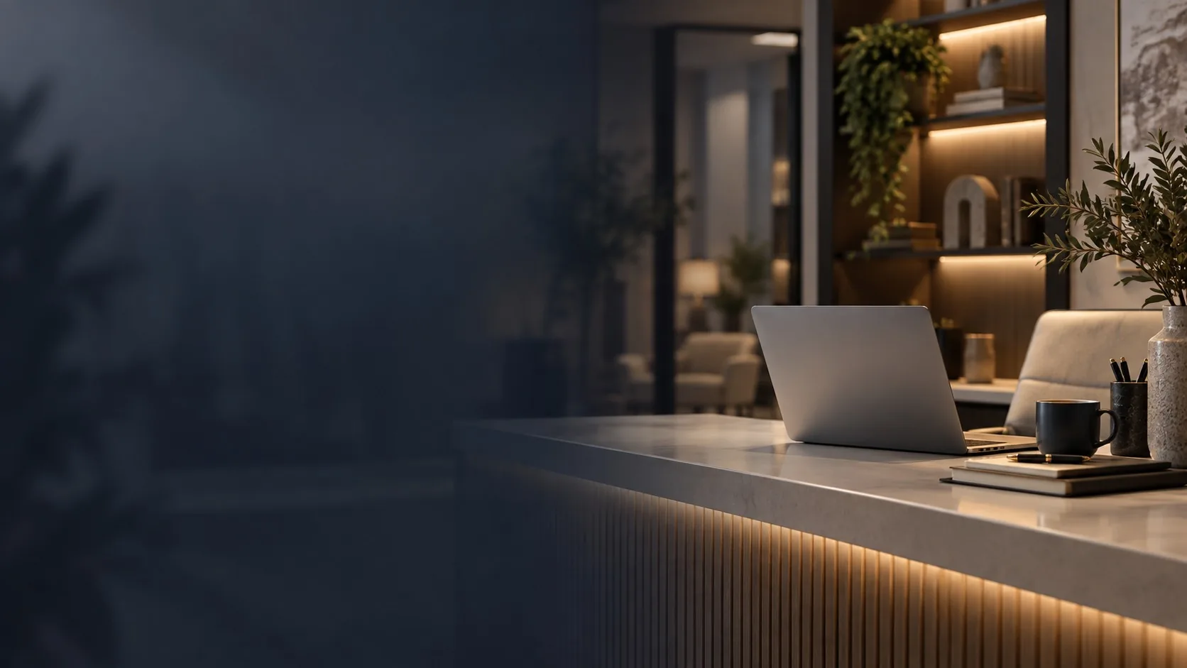 A reception desk after hours, a laptop open on the stone counter under warm shelf lighting